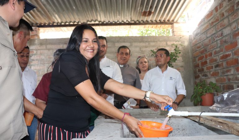 Mujer echando agua en recipiente ante la mirada de un grupo de personas