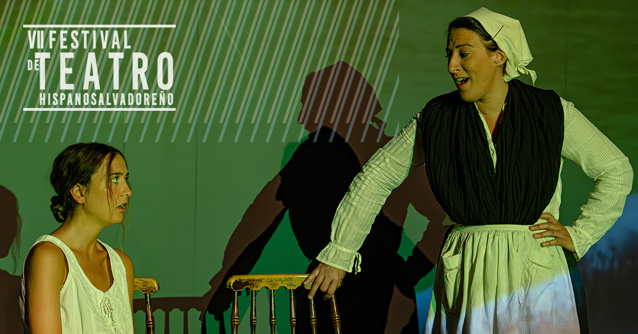 Dos actrices de la obra en el escenario. Una sentada en una silla y la otra, de pie, hablando con ella y vestida como se hacía en el País Vasco hace un siglo. Aparece el texto: VII Festival de Teatro Hispanosalvadoreño.