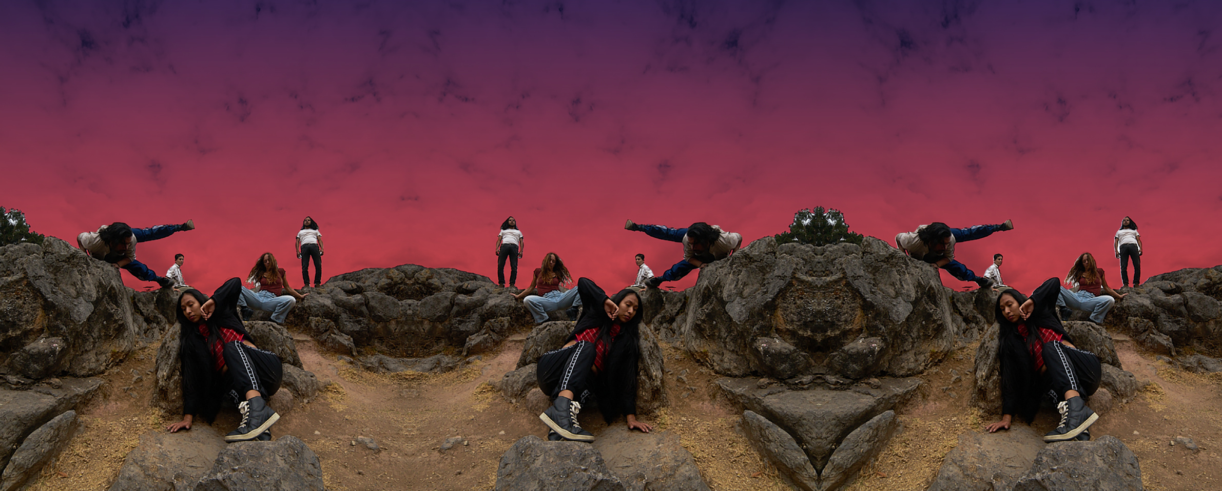 La imagen es una fotografía de varios bailarines y bailarinas que danzan sobre un terreno rocoso y arenoso. Al fondo se ve el cielo rojizo por la caída del sol.