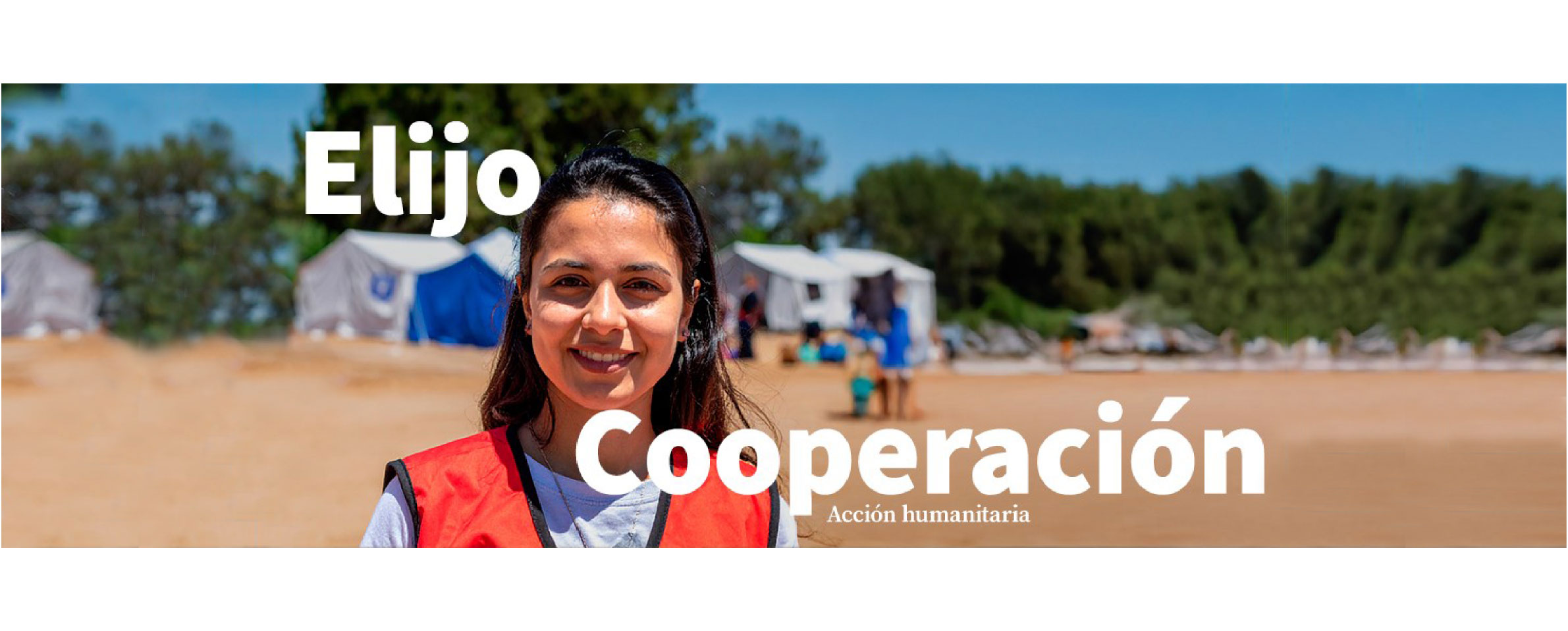 Foto que muestra en primer plano a una joven vestida con un polo blanco y un chaleco rojo. Detrás de ella hay un campamento de ayuda humanitaria con varias carpas blancas y azules. En la imagen se lee ELIJO COOPERACIÓN. Acción Humanitaria. 