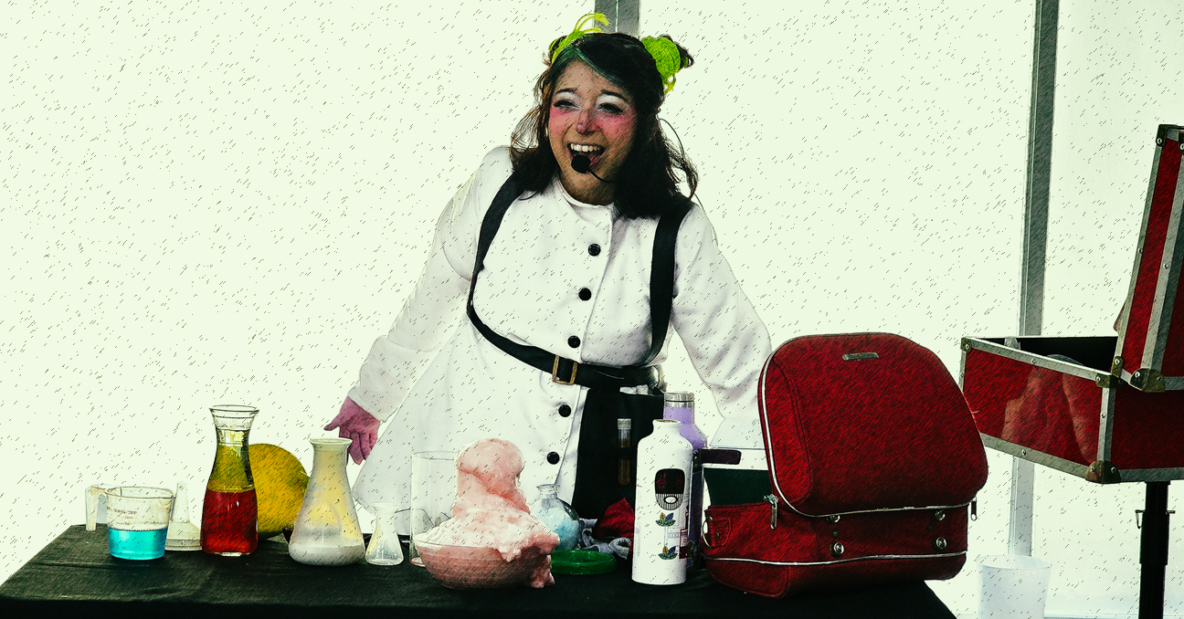 La artista Lala, vestida con bata de científica y maquillaje de payasa, ante una mesa con elementos de laboratorio
