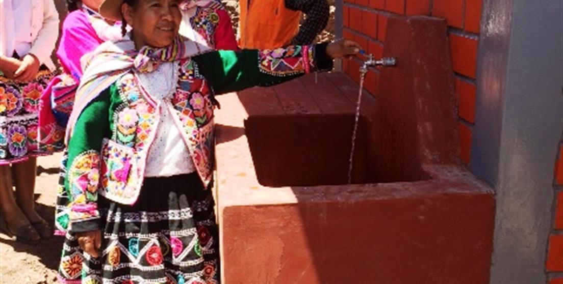 Una mujer abre el grifo ataviada con ropa tradicional