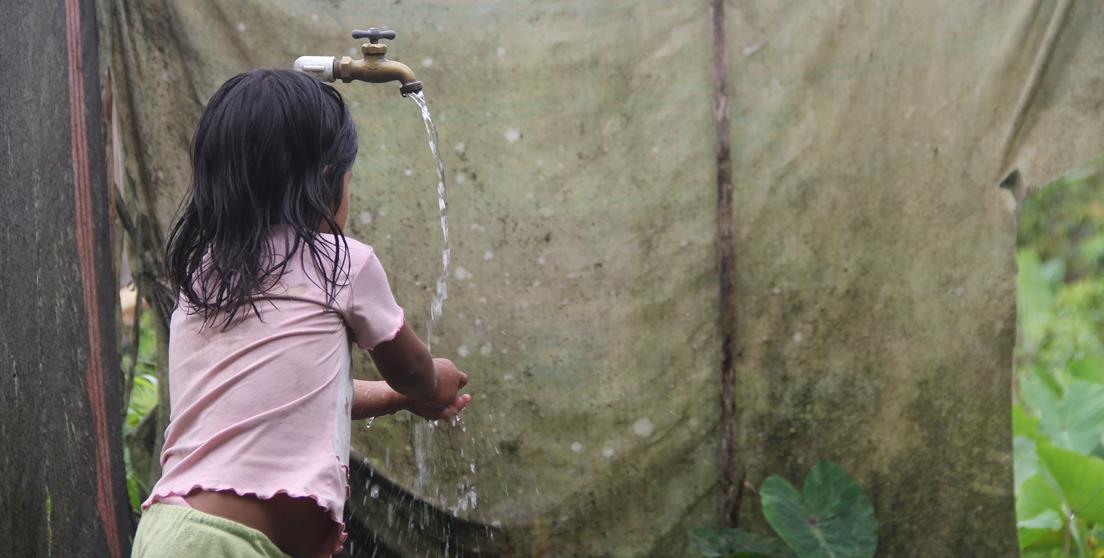 Una niña se lava las manos en un grifo precario